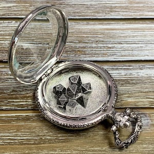 May include: A silver pocket watch with a hinged lid, open to reveal a set of silver metal dice inside. The dice are a d4, d6, d8, d10, d12, and d20.