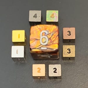 May include: A collection of square dice with numbers 1-6. The central die is a marbled orange and brown color with a white number 6. The other dice are various metallic colors, including gold, silver, and copper. The dice are arranged in a circular pattern.