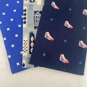May include: Three fabric swatches with different patterns. One is blue with white crosses, another is light blue with architectural illustrations, and the third is navy with red and white sneakers and blue stars.