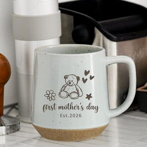 以下が含まれることがあります： テディベアのイラストと「first mother's day」の文字が入った、茶色の底の薄い青色のセラミックマグカップ。 その他、コーヒーグラインダー、タンパー、黒い容器などがあります。