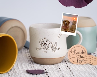 Puede incluir: Una taza de cerámica moteada con base marrón presenta un dibujo lineal de un perro y un gato, con los nombres "Lucky" y "Lulu" debajo. Se adjunta una pequeña foto de un perro y un gato.
