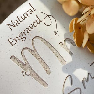 May include: A close-up of a white ceramic surface with the engraved word "Mr" and the last name "Smith". The words "Natural Engraved" are above the name, with a heart symbol. The Etsy shop name "@LoviBrush" is at the bottom.