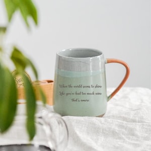 May include: A ceramic mug with a light green base, a gray top, and an orange handle. The mug has the text "When the world seems to shine like you've had too much wine that's amore."