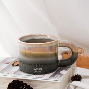 Può includere: Un set di tre tazze in ceramica con una glassa screziata color crema. Ogni tazza presenta un design dipinto a mano diverso: una foglia blu e verde, un fiore giallo e una bacca rossa. Le tazze hanno un design semplice e moderno.