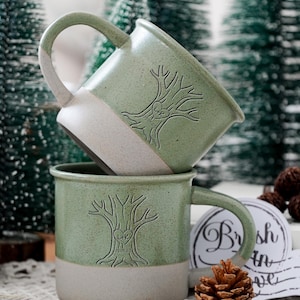 Puede incluir: Dos tazas de cerámica con un diseño de dos tonos que presenta una sección superior de color verde salvia moteado y una base de color beige mate. Cada taza muestra un gráfico de árbol en relieve con un corazón que contiene las letras L+K y la fecha 03.05.23.