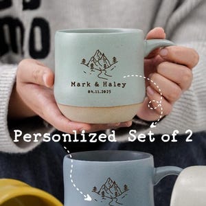 May include: Set of two personalized light blue ceramic mugs with a mountain scene and the text "Mark & Haley 04.11.2025". Each mug has a capacity of 17.5 ounces or 520 milliliters.