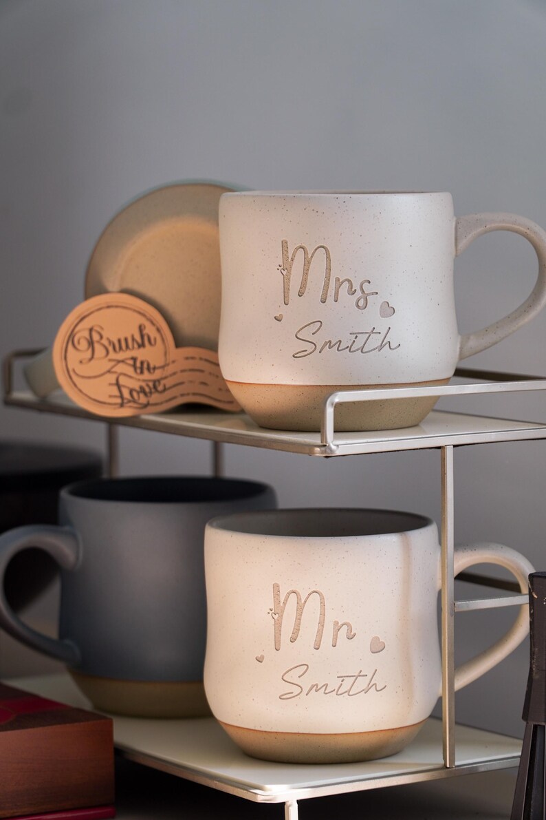 May include: Two ceramic mugs with a rustic finish. The mugs are personalized with the text "Mrs. Smith" and "Mr. Smith".