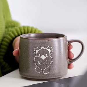 May include: A gray ceramic mug with a koala bear design holding a heart with the letters "W & S" inscribed.
