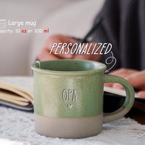 May include: A large, personalized mug with a capacity of 10 oz. The mug is two-toned, with a light green upper half and a beige lower half. The word "OPA" is etched on the front, with a small heart below. The word "PERSONALIZED" is written above the mug.