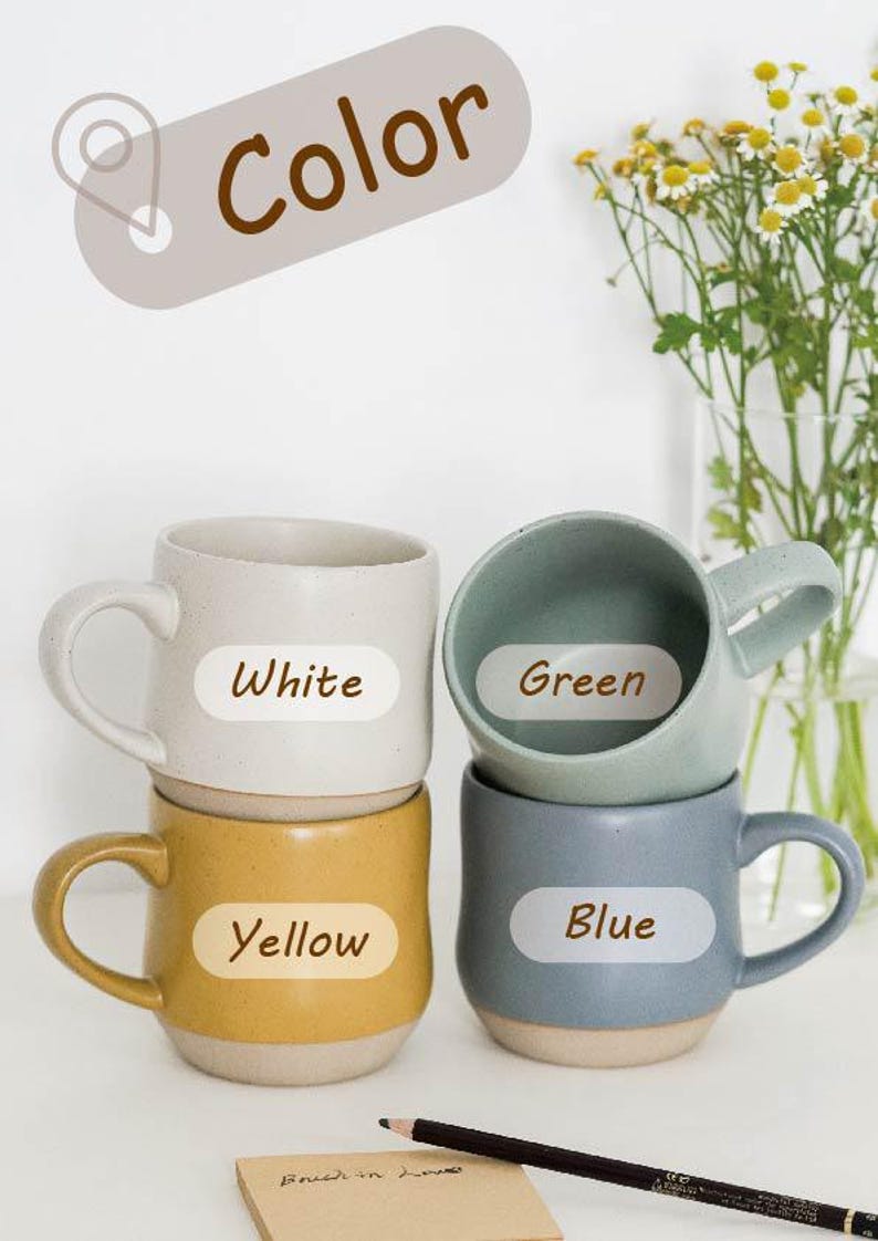 May include: Four ceramic mugs stacked on top of each other. The mugs are white, green, yellow, and blue. Each mug has a label with the color of the mug written on it.