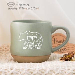 Könnte beinhalten: Eine grüne Keramiktasse mit braunem Boden. Die Tasse zeigt eine weiße Bärensilhouette mit dem Wort "papa" darin. Die Tasse hat ein Fassungsvermögen von 520 ml.