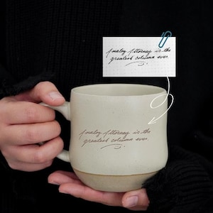 Może przedstawiać: Kremowy ceramiczny kubek z brązową podstawą, z ręcznie napisanym tekstem "Analog Attorney is the greatest column ever". Mały papier z tym samym tekstem jest przymocowany spinaczem. Kubek ma zakrzywiony uchwyt.