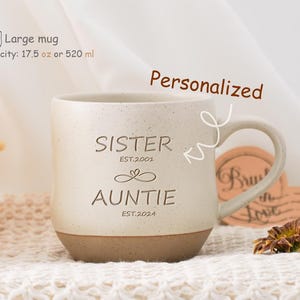 May include: White ceramic mug with a brown rim. The mug has the text "Sister Est. 2001" and "Auntie Est. 2024" printed on it. The mug is 17.5 ounces or 520 millilitres.