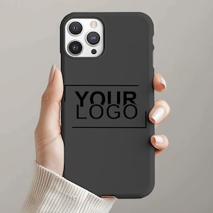 Op de afbeelding: Zwarte telefoonhoes met de tekst "YOUR LOGO" in zwart in een rechthoekige vorm. De hoes heeft een matte afwerking en is ontworpen voor een smartphone. De telefoonhoes wordt in de hand van een persoon gehouden.