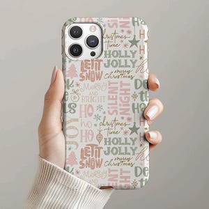 Puede incluir: Una funda de teléfono con un tema navideño festivo. La funda presenta un patrón repetido de palabras festivas como "JOY", "HOLLY" y "SNOW", junto con estrellas, copos de nieve y árboles de Navidad en tonos rosa, verde y blanco.