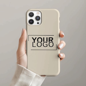 May include: A beige phone case with the text "YOUR LOGO" in black. The case has a rectangular design and a camera cutout. The phone case is held by a person.