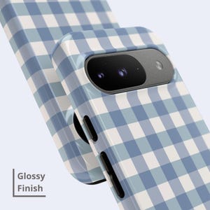 May include: A smartphone case featuring a light blue and white gingham check pattern with a glossy finish. The case has a cutout for the camera module and black side buttons. The text "Glossy Finish" is printed in the lower left corner.