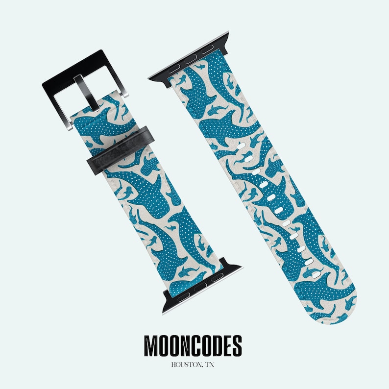 May include: Two-piece watch strap featuring a blue whale shark design on a light beige backdrop. The strap has a black buckle and connectors. The brand name "MOONCODES" and location "HOUSTON, TX" are printed at the bottom.