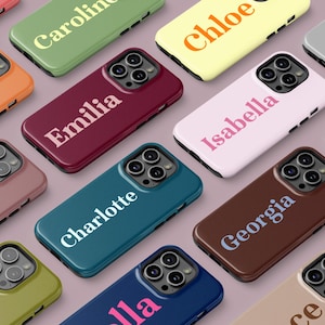 May include: A selection of mobile phone cases in various colours, each displaying a different name. The cases are in shades like pink, orange, green, and blue. The names are printed in a contrasting colour, such as white or light pink.