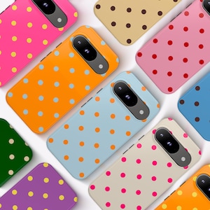 May include: A collection of smartphone cases featuring various solid background colors including hot pink, orange, light blue, beige, purple, and dark green, each decorated with a repeating pattern of contrasting polka dots and a black camera cutout.