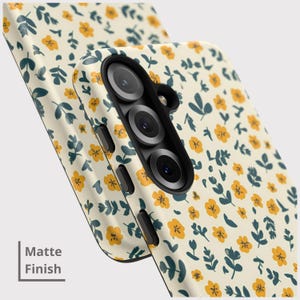 May include: A phone case with a matte finish, featuring a repeating pattern of small yellow flowers and dark teal leaves on a cream background. The case has a black camera module and side buttons. The text "Matte Finish" is visible.