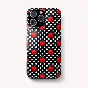 Puede incluir: Una funda de teléfono negra con un patrón de lunares blancos y mariquitas rojas. La funda tiene un acabado brillante y un recorte para la cámara. Las mariquitas están espaciadas uniformemente.
