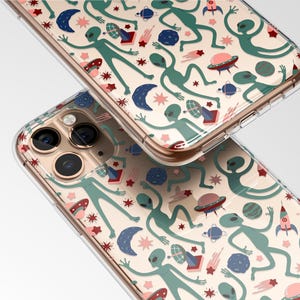 May include: Two clear phone cases with a repeating pattern of green aliens, planets, rockets, and stars. The design includes pink, blue, and red accents on a cream background. The cases are slightly angled, showcasing the design.