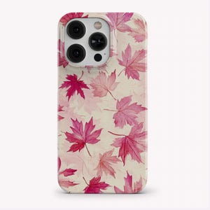 Puede incluir: Una funda para smartphone con un patrón repetitivo de hojas de arce estilo acuarela en varios tonos de rosa y magenta sobre un fondo color crema. La funda tiene un recorte para un sistema de cámara de tres lentes.