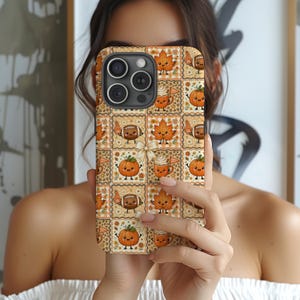 Puede incluir: Una funda para teléfono con un patrón de cuadrícula repetitivo de ilustraciones con temática otoñal que incluye calabazas sonrientes, hojas de arce, balones de fútbol con dedos de espuma y tazas de café con crema batida sobre un fondo beige.
