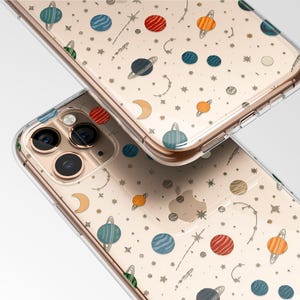 May include: Clear phone cases with a repeating pattern of colorful planets, stars, and crescent moons. The cases are designed to fit a smartphone, with cutouts for the camera and buttons. The design features planets in shades of blue, orange, and red.