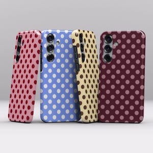 Op de afbeelding: Vier smartphonehoesjes op een rij, elk met een verschillend stippenpatroon. De hoesjes zijn uitgevoerd in lichtroze met rode stippen, lichtblauw met witte stippen, crème met bruine stippen en donkerrood met lichtroze stippen.