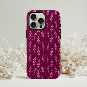 Puede incluir: Funda de teléfono burdeos con un patrón repetido de hojas de color rosa claro y pequeños puntos. La funda tiene un recorte para la cámara y un borde negro. El diseño es de temática floral y botánica.