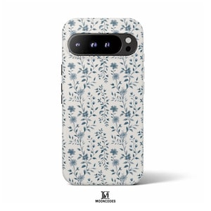 Könnte beinhalten: Eine Handyhülle mit floralem Muster. Die Hülle hat einen weißen Hintergrund mit einem sich wiederholenden Muster aus blauen Blumen und Blättern. Die Kamera und der Blitz des Telefons sind oben sichtbar. Der Markenname "MOONCODES" steht unten.