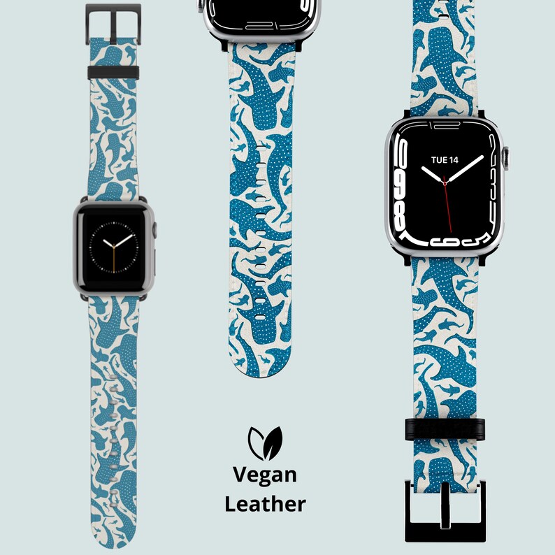 May include: Three Apple Watch straps featuring a blue whale shark design on a cream backdrop. The straps are made of vegan leather and have black buckles. The watch faces show the time and date.