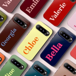 May include: A collection of personalized phone cases in various colors, including brown, yellow, and blue. Each case features a different name in a contrasting color, such as "Georgia" in blue and "Chloe" in orange. The cases have a sleek, modern design.