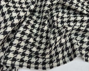 May include: Close-up of a fabric with a black and white houndstooth pattern. The fabric is draped, showing the texture and design. The classic pattern is repeated across the material.