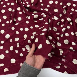 A hand is holding a piece of fabric with a maroon color and white polka dots.