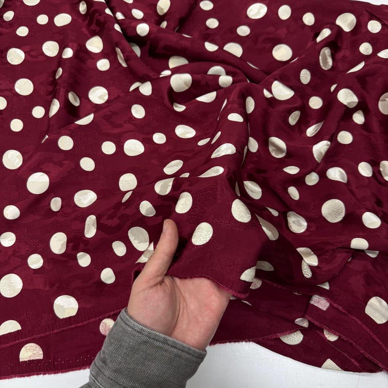 A hand is holding a piece of fabric with a maroon color and white polka dots.