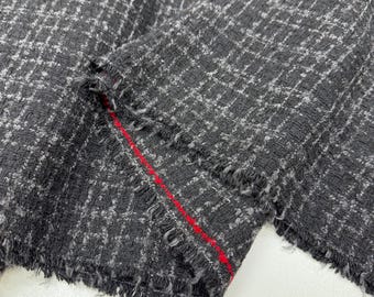 May include: Close-up of a textured fabric with a black and grey chequered pattern. The fabric has a frayed edge and a red stitch detail. The material appears to be a woven textile, possibly for clothing or upholstery.