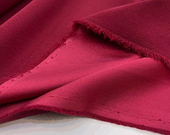 May include: Close-up of a deep red fabric with a smooth, silky texture. The fabric is folded over, showing the edges and a subtle sheen.