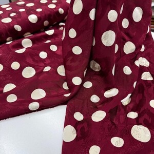 a close-up view of a fabric with a maroon color and white polka dots. The fabric appears to be a piece of clothing or textile with a pattern of white polka dots on a maroon background.