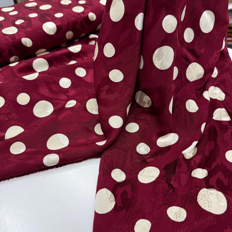 a close-up view of a fabric with a maroon color and white polka dots. The fabric appears to be a piece of clothing or textile with a pattern of white polka dots on a maroon background.
