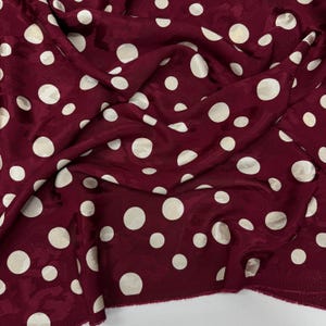 a close-up view of a fabric with a maroon color and white polka dots. The fabric appears to be crumpled and wrinkled, giving it a casual and relaxed appearance.