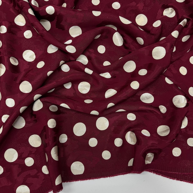 a close-up view of a fabric with a maroon color and white polka dots. The fabric appears to be crumpled and wrinkled, giving it a casual and relaxed appearance.