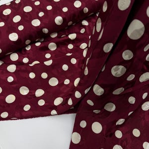 a close-up view of a fabric with a maroon color and white polka dots. The fabric appears to be a piece of clothing or textile with a pattern of white polka dots on a maroon background.