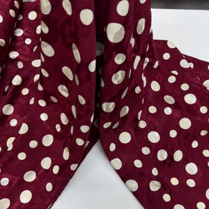 a close-up view of a fabric with a maroon color and white polka dots. The fabric appears to be a piece of clothing or textile, with the polka dots covering the entire surface.