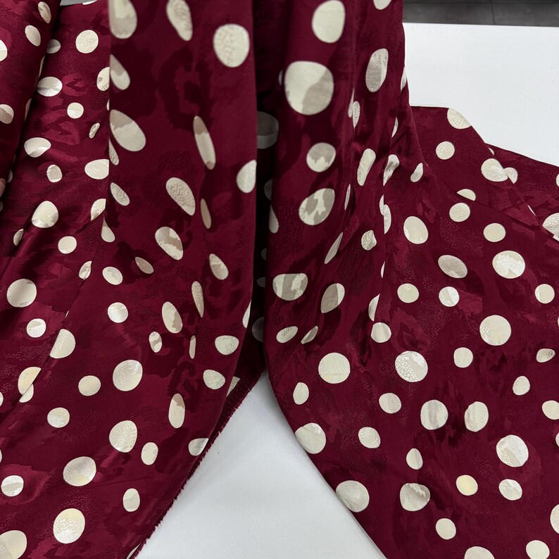 a close-up view of a fabric with a maroon color and white polka dots. The fabric appears to be a piece of clothing or textile, with the polka dots covering the entire surface.