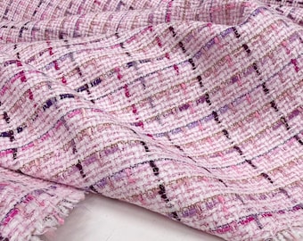 Op de afbeelding: Close-up van een roze tweed stof met een geweven ruitpatroon. De stof heeft een mix van roze, paarse en zwarte draden, waardoor een textuur ontstaat. De randen zijn gerafeld, wat de constructie van de stof laat zien.