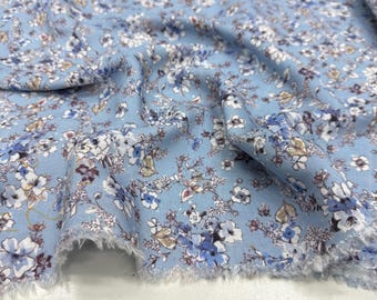May include: Light blue floral fabric with a delicate pattern of white, blue, and brown flowers. The fabric has a soft, textured appearance and a frayed edge, suggesting it's cut from a larger piece. Ideal for sewing projects.