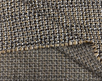 Op de afbeelding: Close-up van een textiel met een geweven patroon. De stof heeft een mix van bruine, zwarte, witte en tan draden, waardoor een tweed-achtige uitstraling ontstaat. De randen zijn gerafeld, waardoor de constructie van de stof zichtbaar wordt. Ideaal voor kleding en woondecoratie.